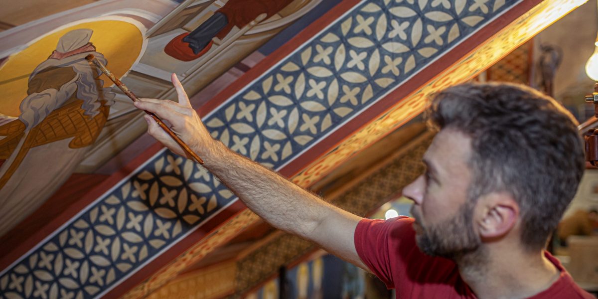 A young painter with a brush in his hand paints details on the Orthodox Church walls